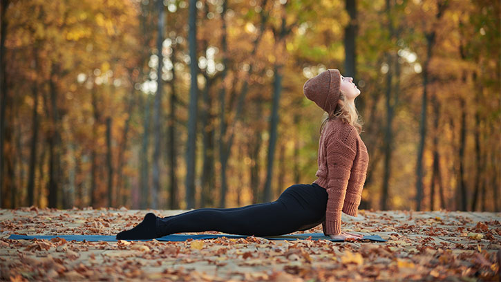Young woman doing cobra posture in an autumn woods