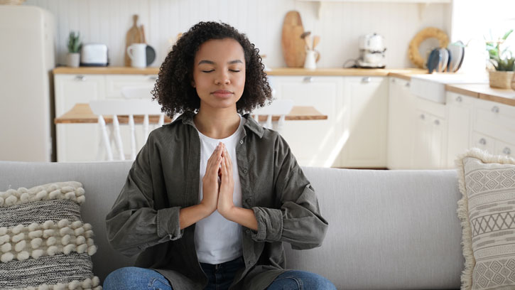 young woman meditating on couch in prayer/namaste posture